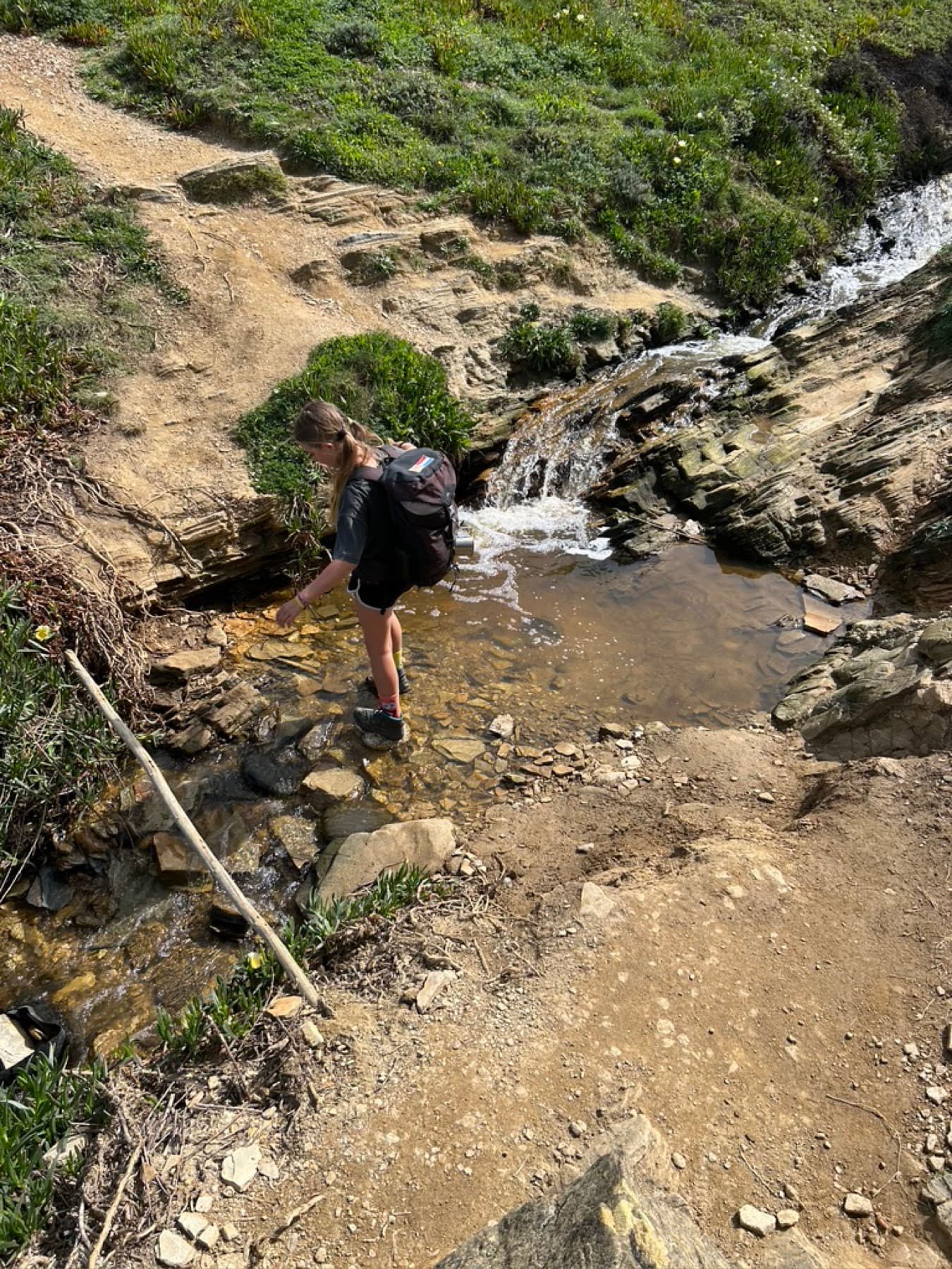 A child crossing a stream on the trail with a backpack